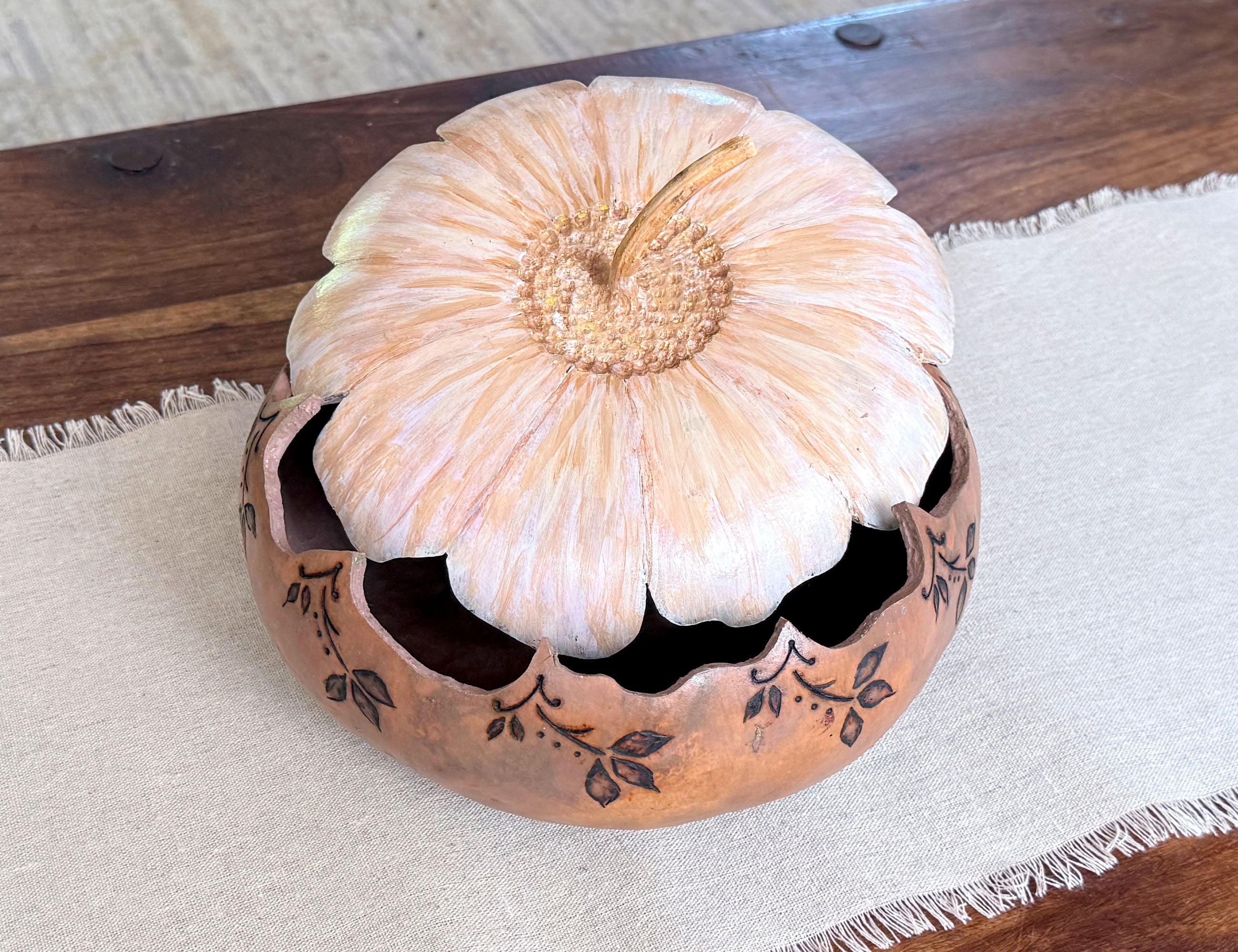 Decorative gourd bowl sitting on a coffee table with the flower blossom lid sitting ajar. 