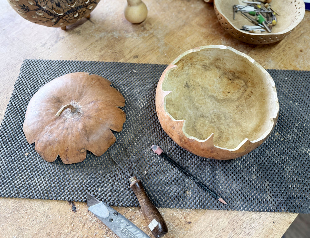 Dried gourd sitting on a work table. The round gourd has the top cut off that is now a lid sitting next to it. Tools lay near.