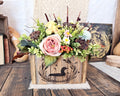 Floral arrangement in a handcrafted wooden box with a wood burned loon design on a rustic wooden surface.