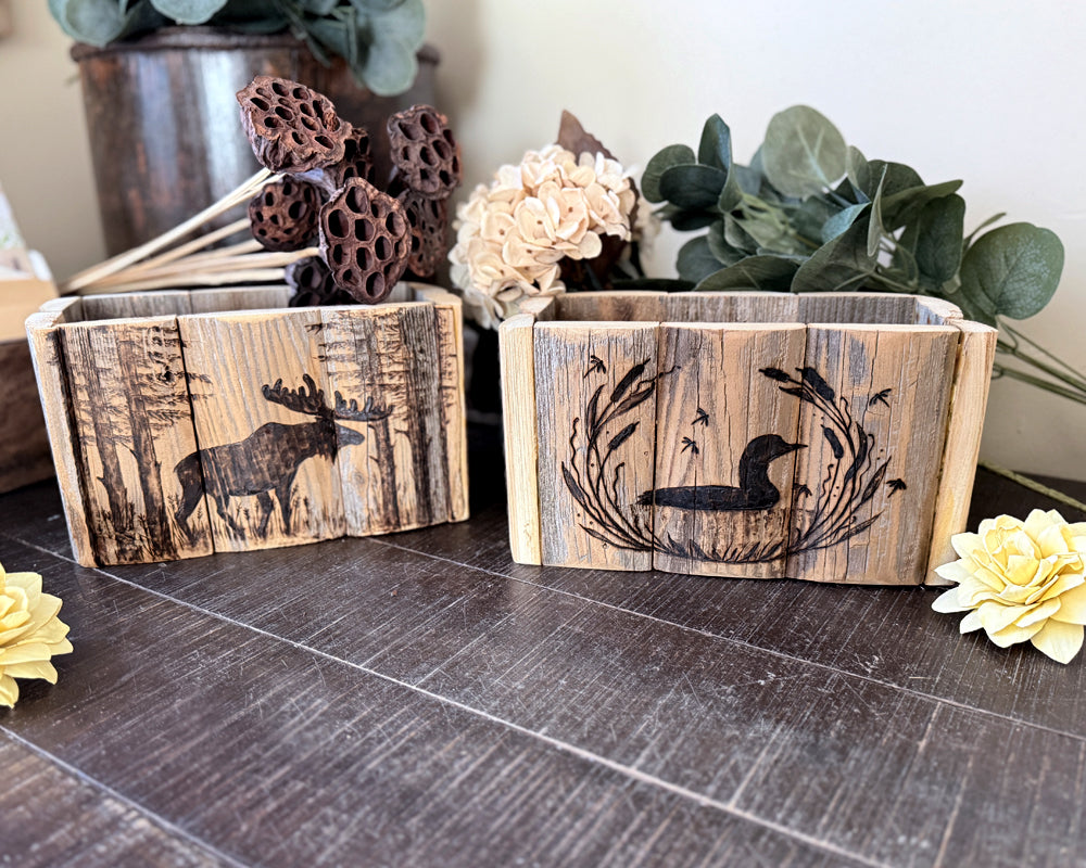 Two handcrafted wooden planters with engraved animals on a wood table.