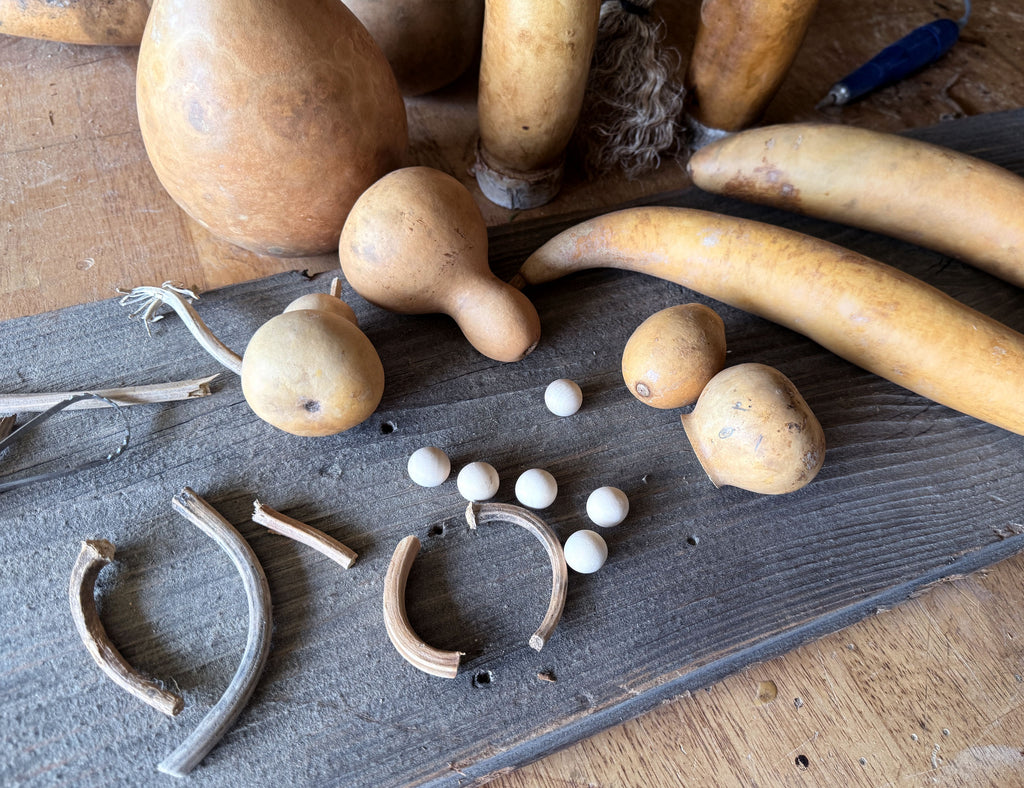 Natural dried gourds and gourd parts arranged on a dark wooden board, with small white beads nearby on a rustic wooden surface.