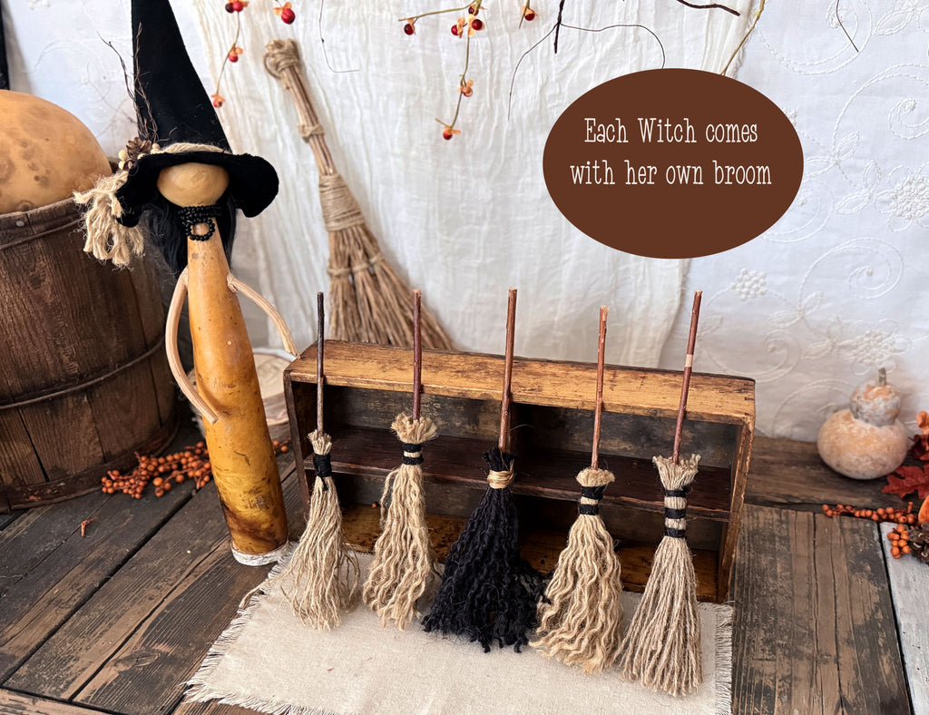 A primitive witch wit pointy hat. Five brooms are leaning against a wood box.