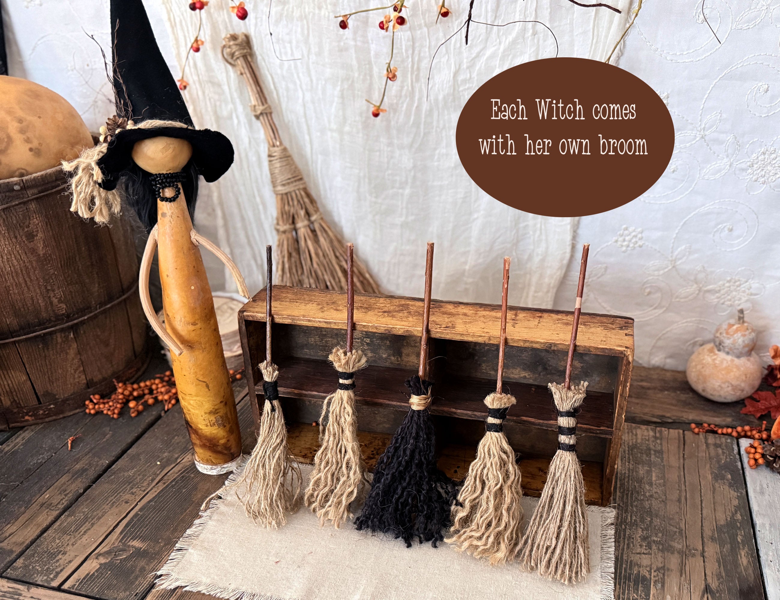 A primitive witch wit pointy hat. Five brooms are leaning against a wood box.