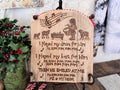A wood wall sign made from upcycled wood with a rounded top. Artwork features the Little Drummer Boy standing near the baby Jesus with sheep near. Musical notes are at the top, with words from the song lyrics below. The artwork has  been wood burned onto the wood.  The top has red and white cord attached with rusty jingle bells. A bouquet of holly berries sits to the left. 