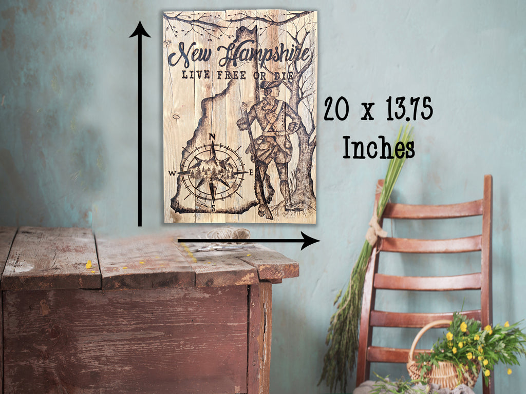 A rustic wooden wall art print featuring an illustration of New Hampshire with the text 'New Hampshire Live Free or Die' and a compass rose, shown hanging on a blue wall above a wooden table. Black arrows and text indicate dimensions of 20 x 13.