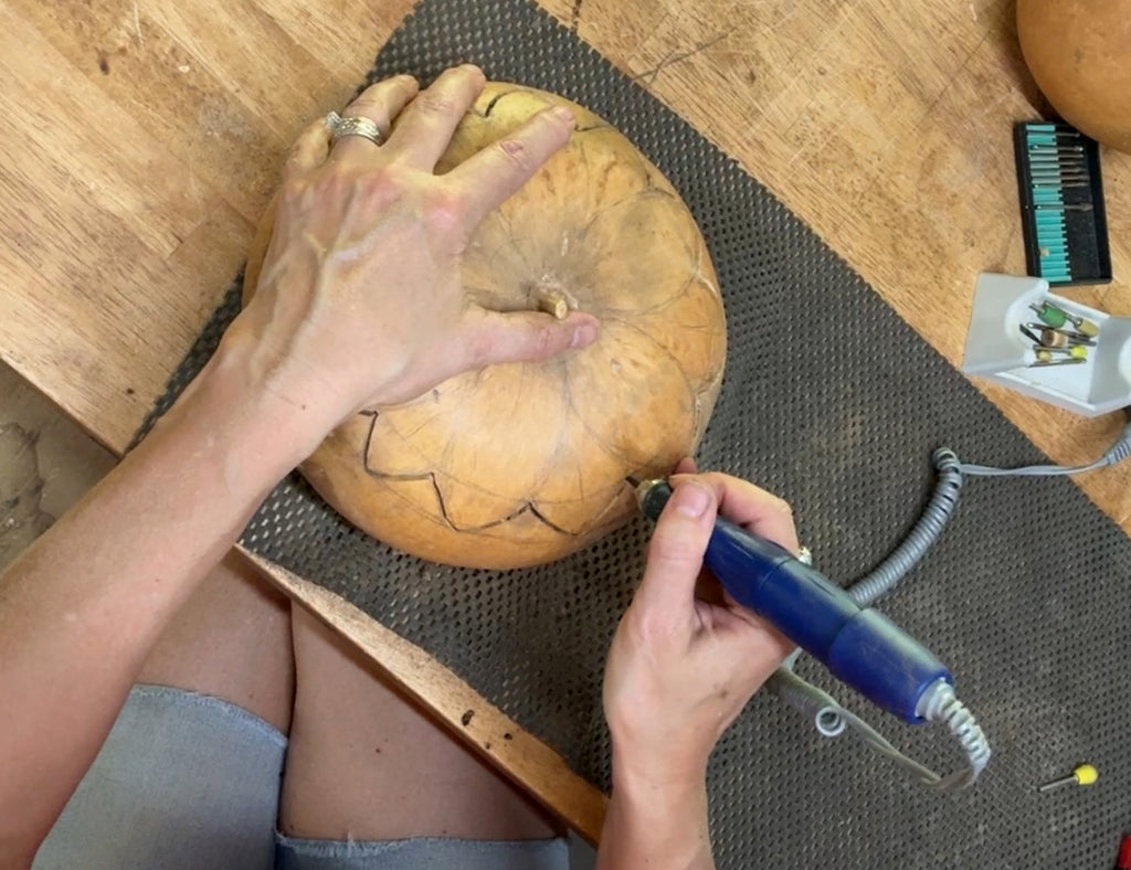Person carving a pumpkin with a blue tool on a wooden table.