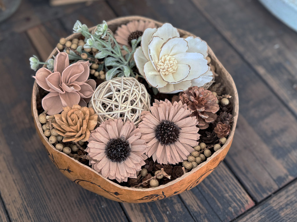 Decorative arrangement of flowers and plants in a natural gourd bowl on a wooden table
