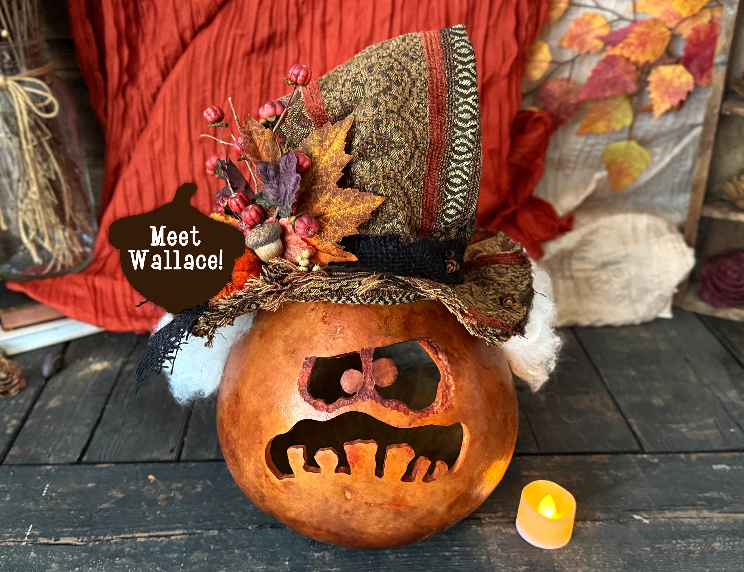 Decorative pumpkin ghost with a hat and candle on a wooden surface
