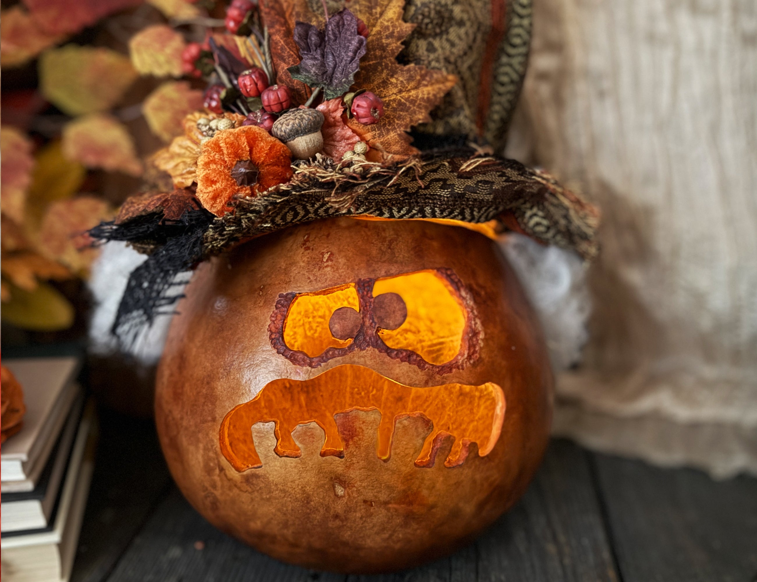 Decorative pumpkin with a face carving and autumn leaves on top, set against a rustic background.