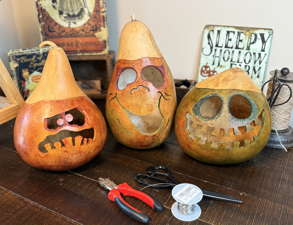 Three gourd carvings with faces on a wooden surface, surrounded by carving tools and a 'Sleepy Hollow' sign.