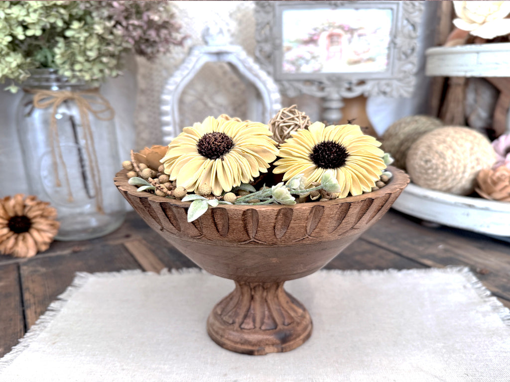 Decorative wooden bowl with yellow flowers on a rustic wooden table.