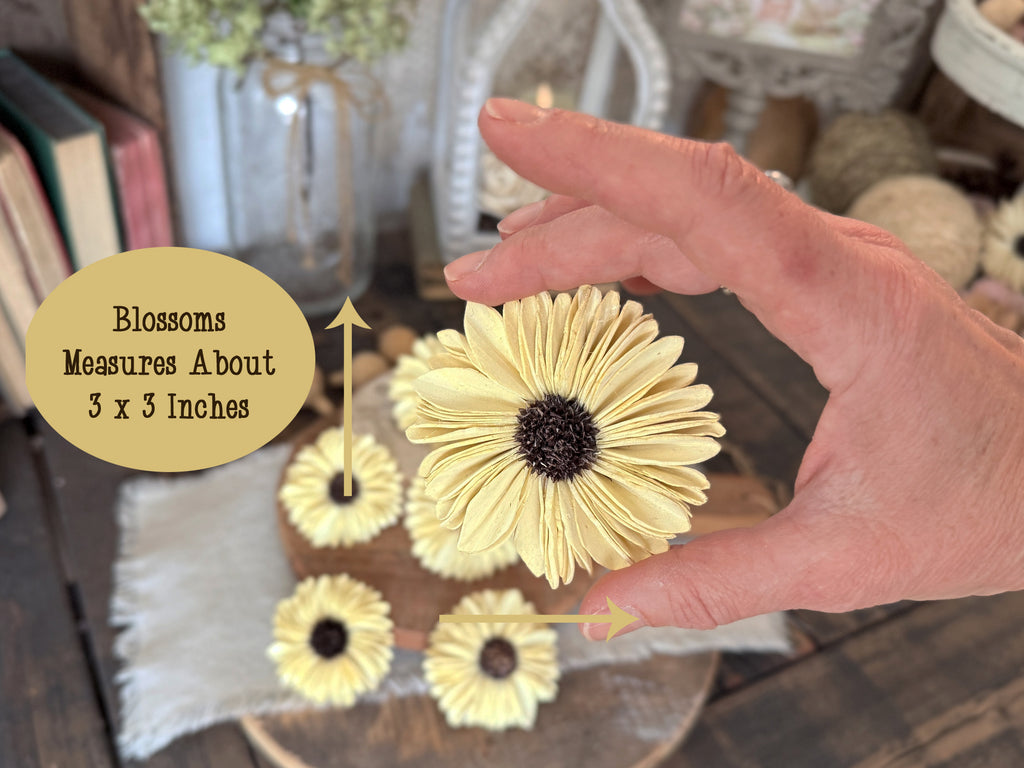 Hand holding a yellow faux flower with text indicating size, set against a blurred indoor background.