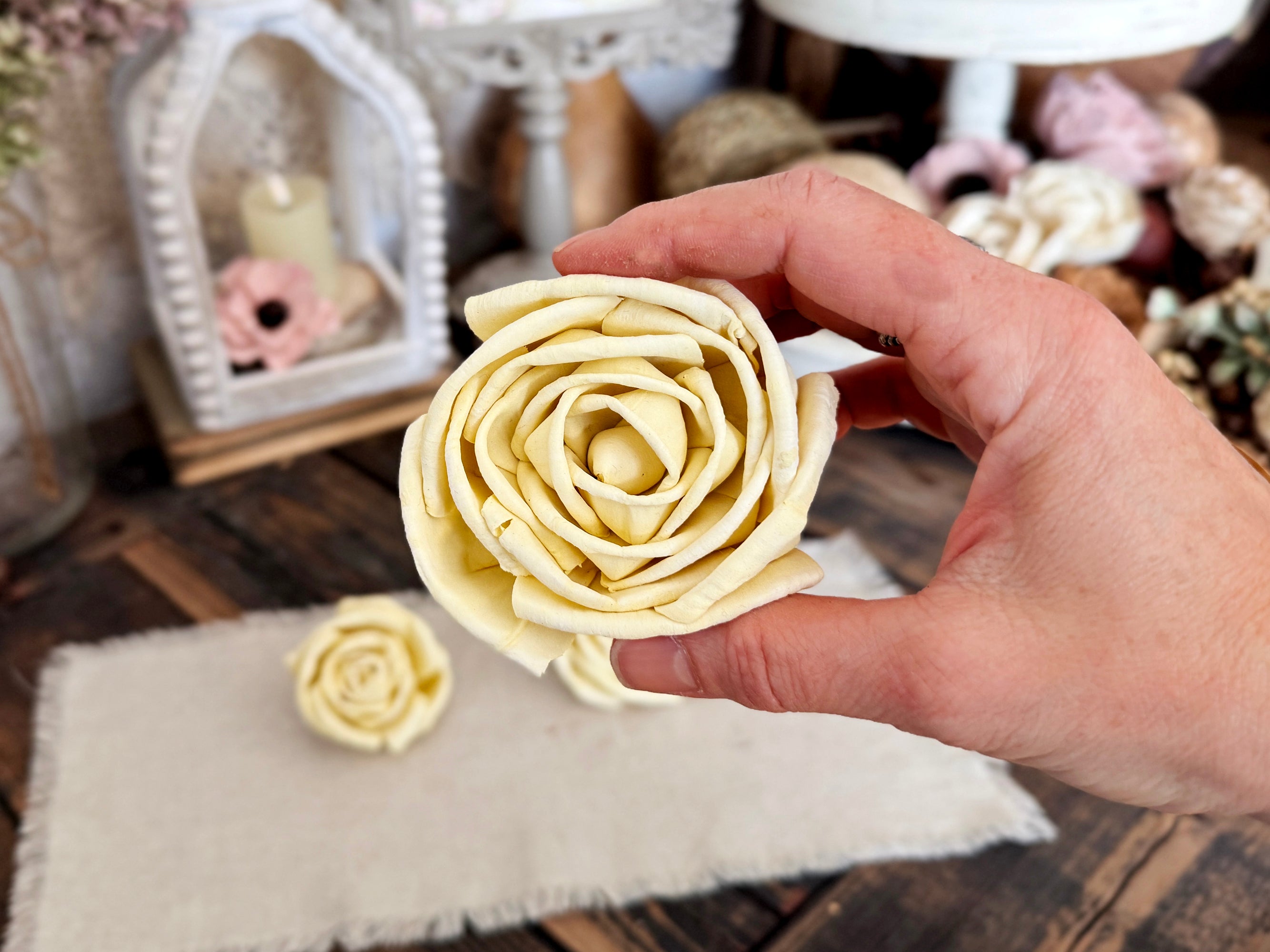 Hand holding a wood rose in a soft butter yellow color. 
