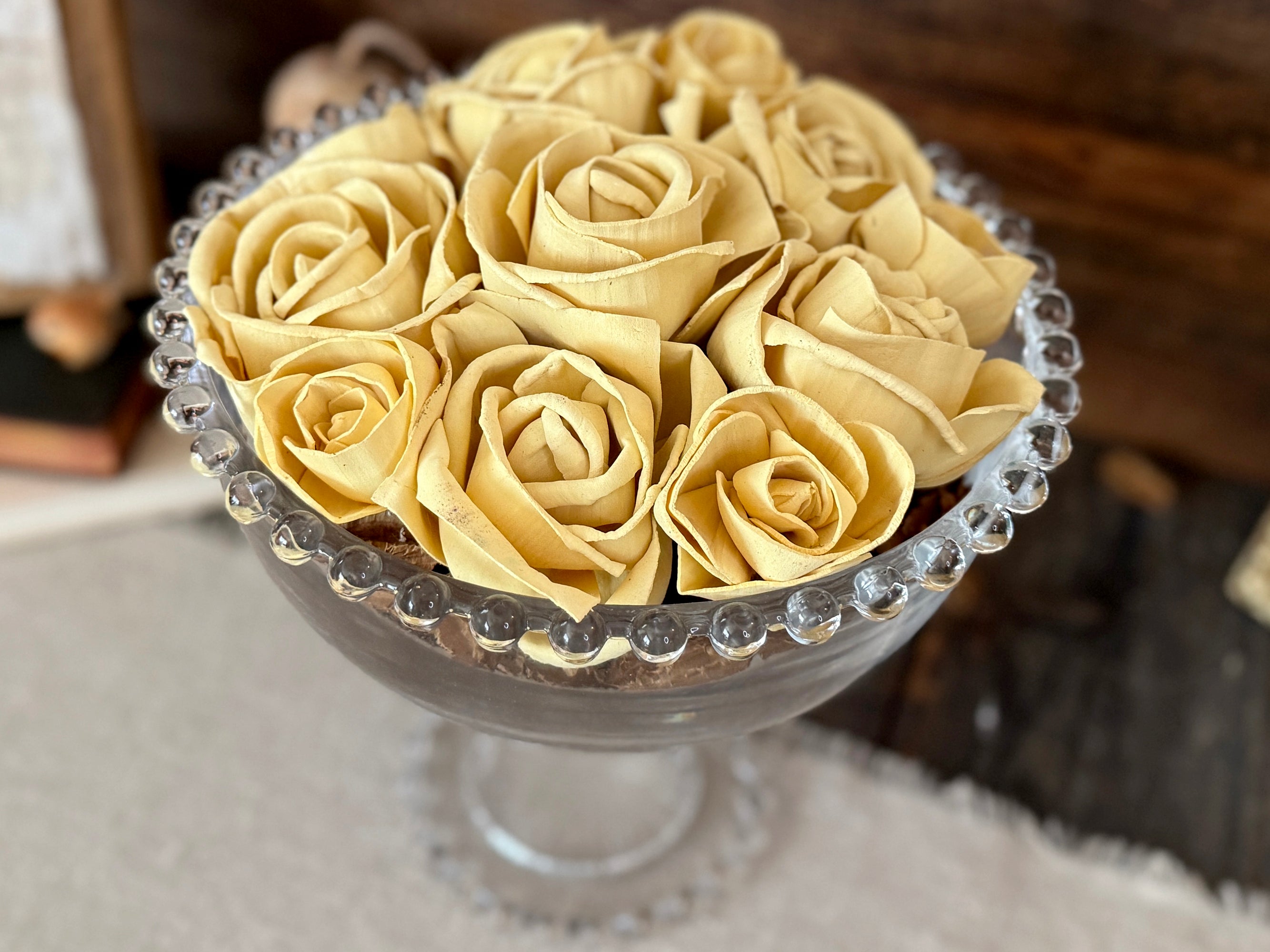 Arrangement of yellow roses in a decorative glass bowl with riser on a textured surface.