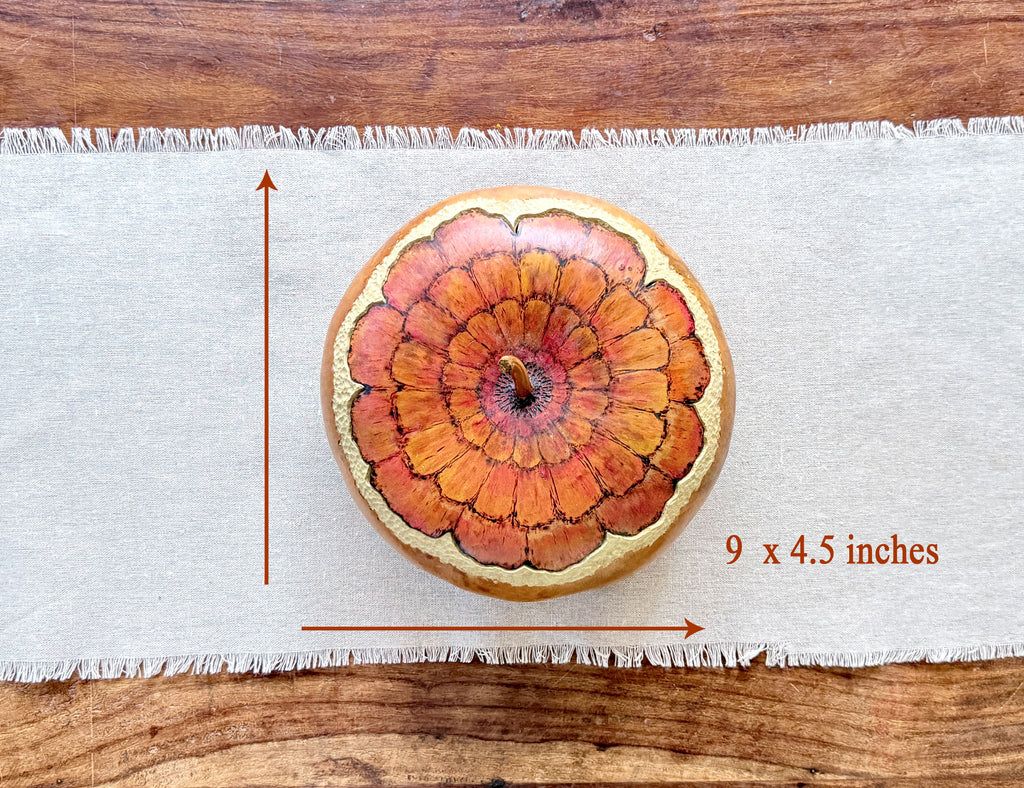 A round decorative gourd bowl with a fitted lid. painted zinnia flower blossom, shown on a white fringed runner over a wooden surface. Red measurement arrows and the text '9 x 4.