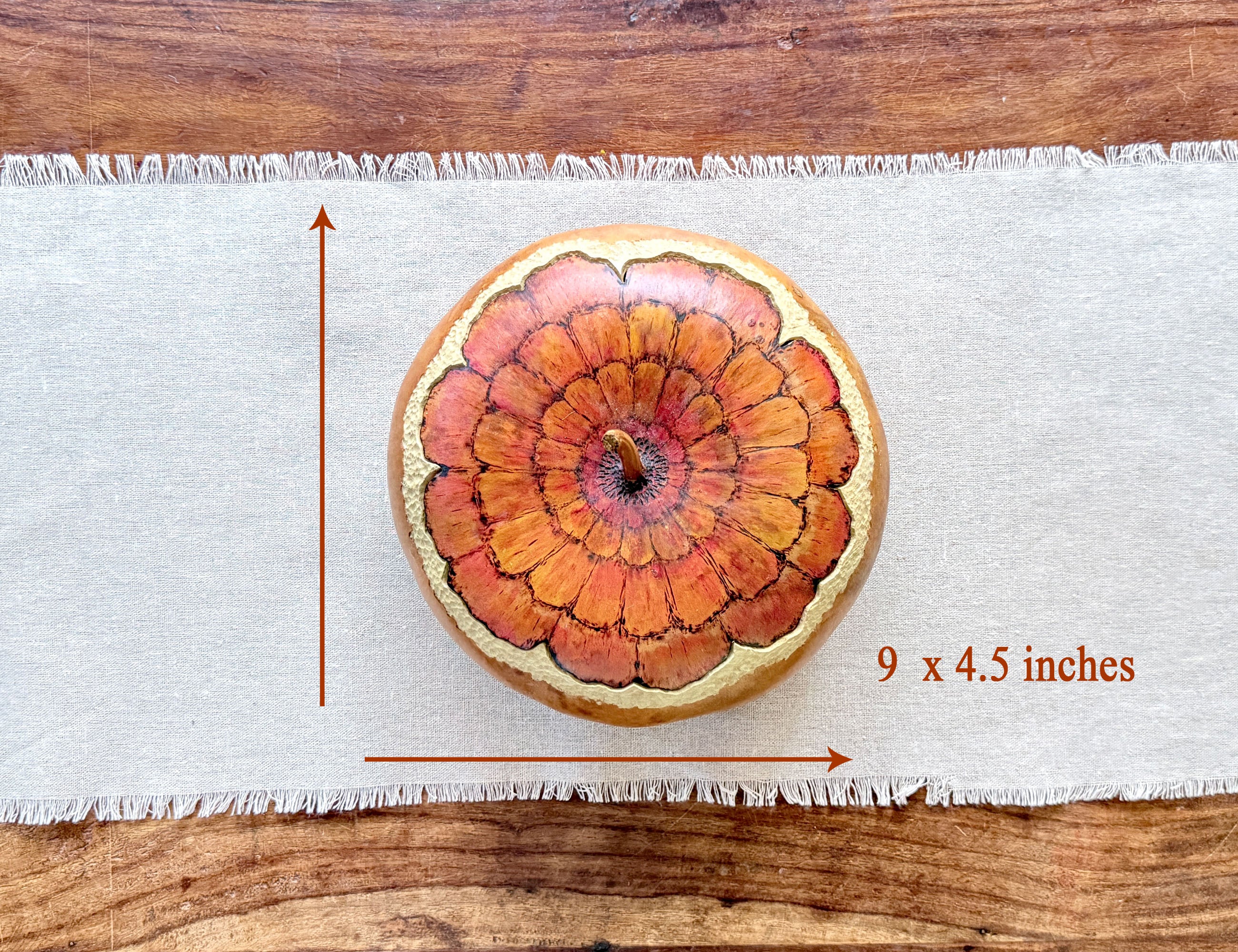 A round decorative gourd bowl with a fitted lid. painted zinnia flower blossom, shown on a white fringed runner over a wooden surface. Red measurement arrows and the text '9 x 4.