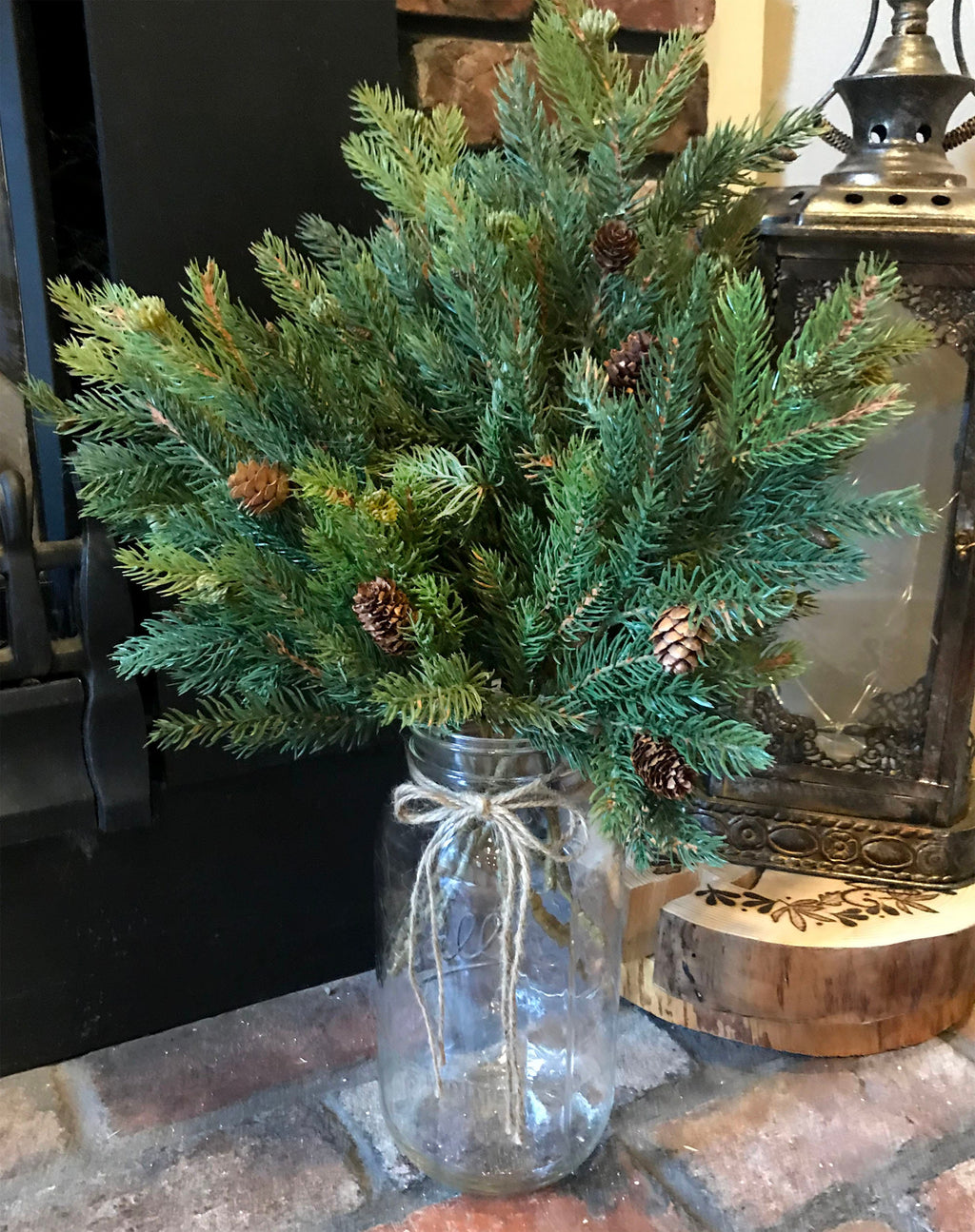 Bouquet of greenery in a mason glass jar with a decorative bow on a stone surface.