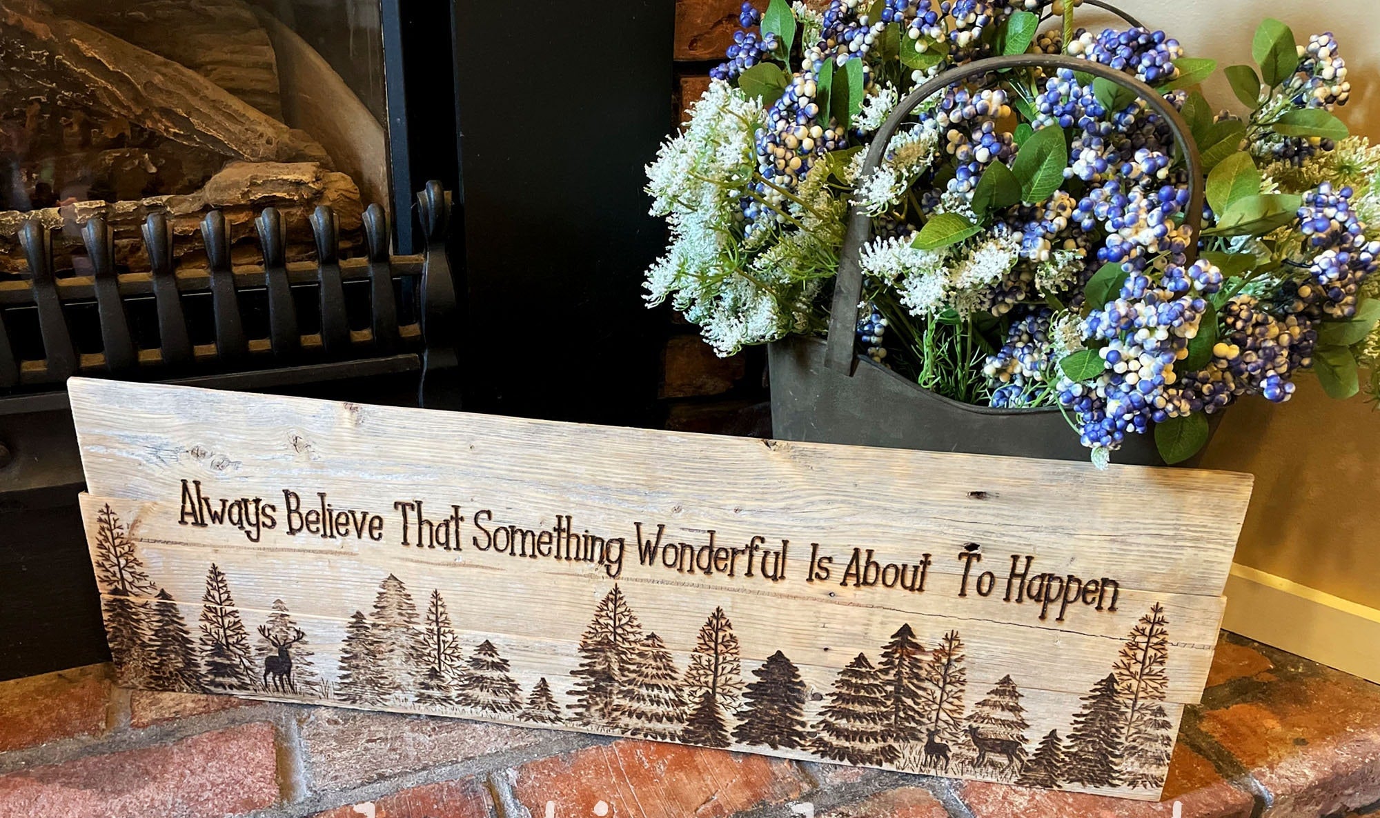 Wooden sign with engraved text and tree design on a brick surface, with a potted plant in the background.