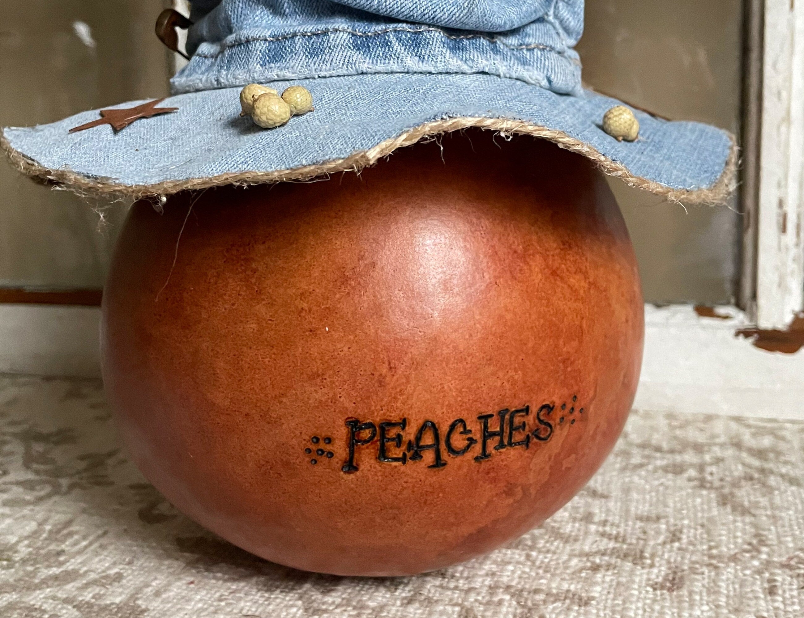 Decorative gourd with 'peaches' text and denim hat on a textured surface
