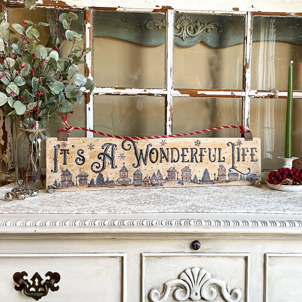 Decorative sign with 'It's a Wonderful Life' text on a vintage cabinet with Christmas decorations.