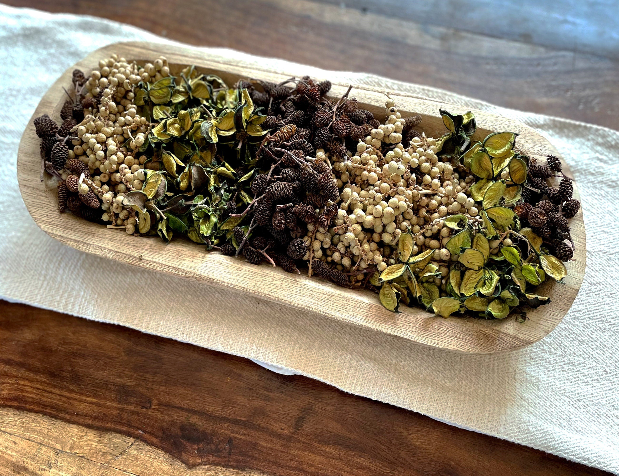 Wooden dough bowl with dried herbs and spices on a coffee table.