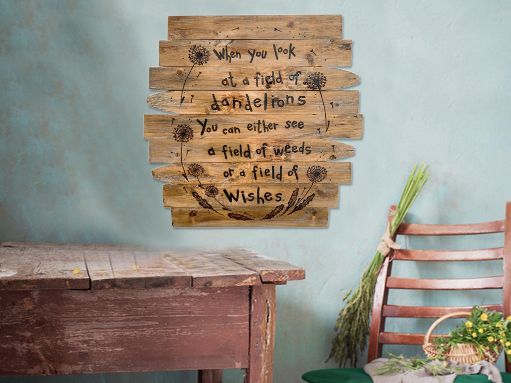 Wooden wall art with a inspirational quote on a light blue wall, with a rustic wooden table and chair in the foreground.