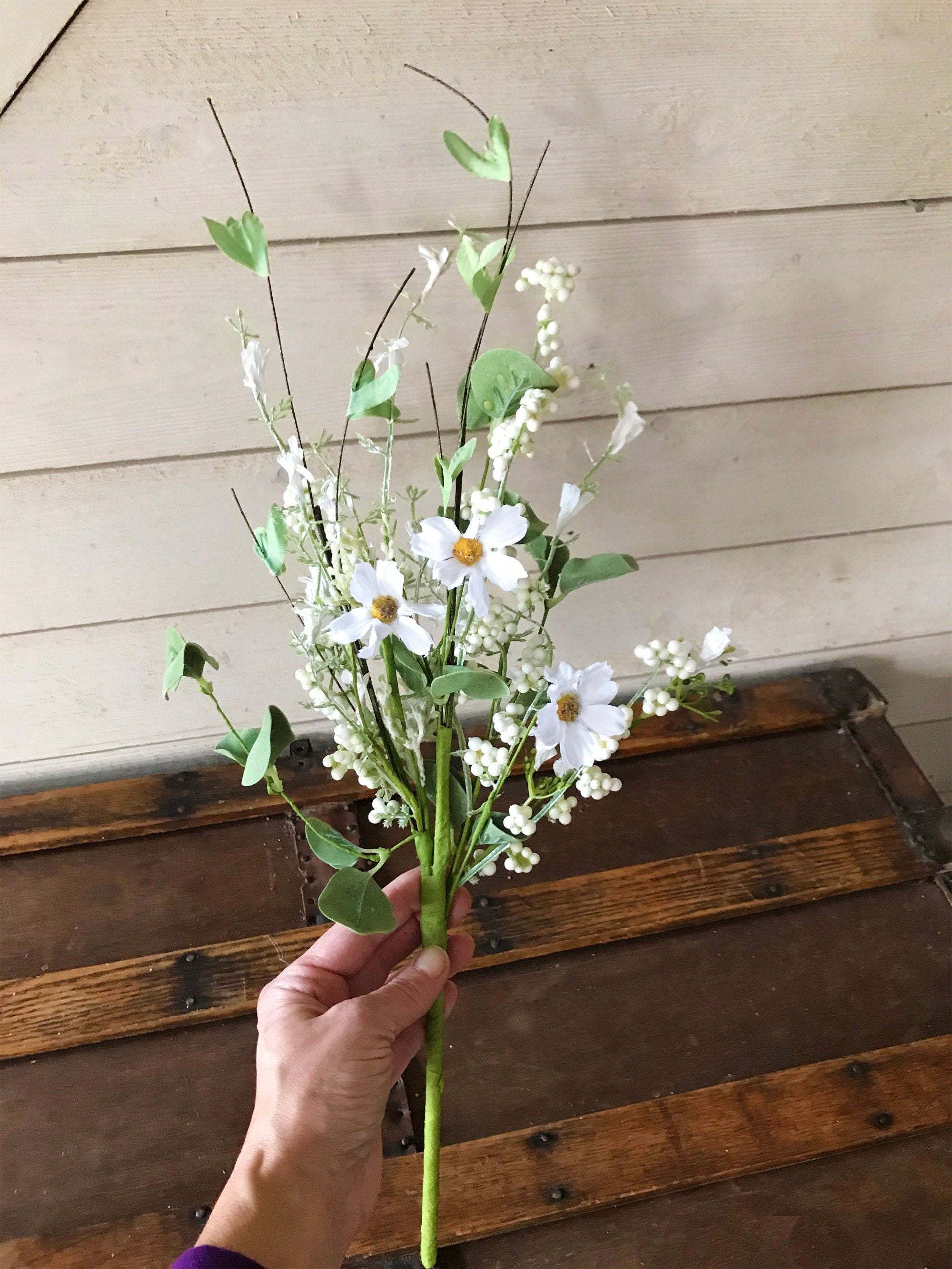 Hand holding a bouquet of white flowers against a wooden background