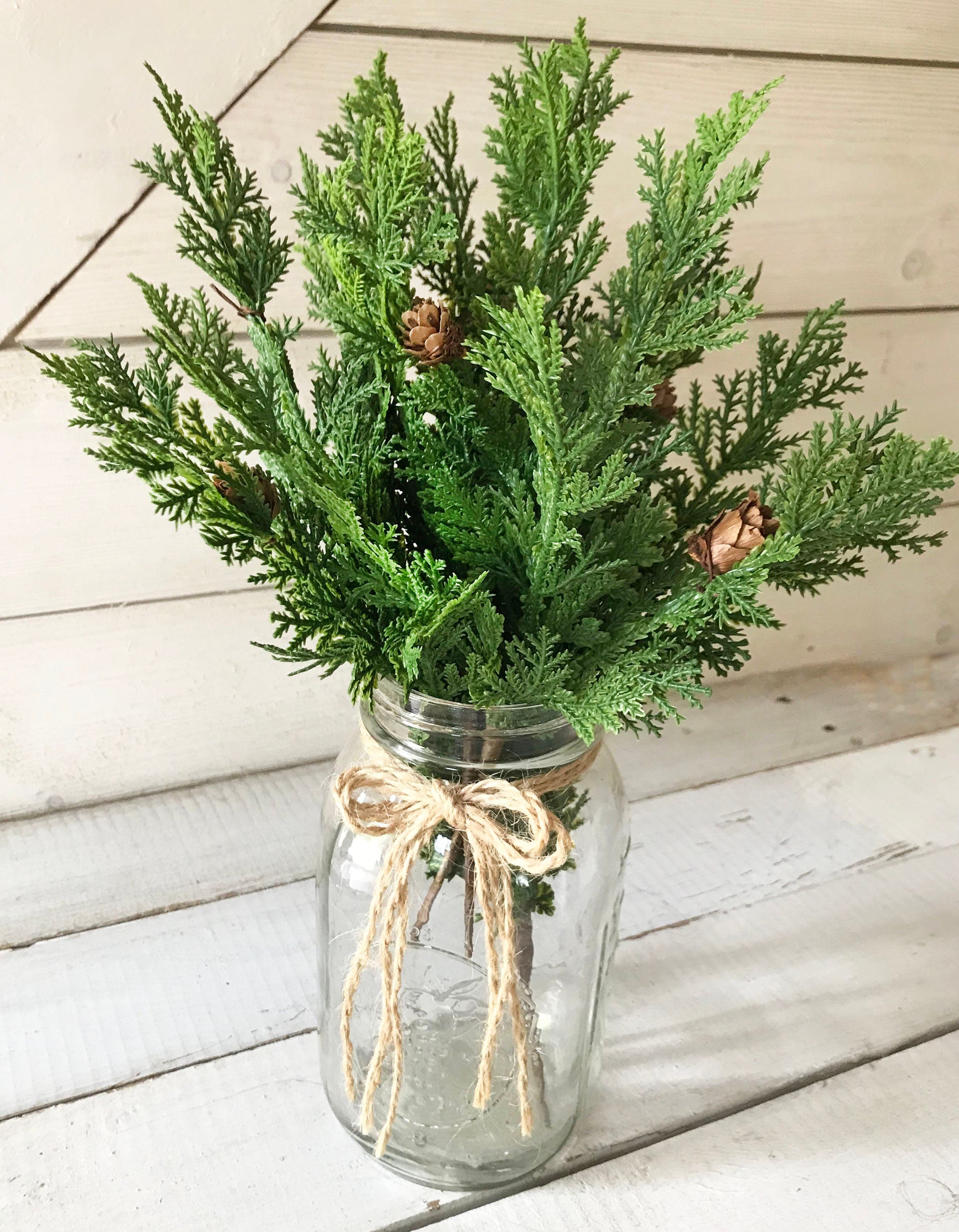 Clear glass jar with greenery and pinecones on a wooden surface