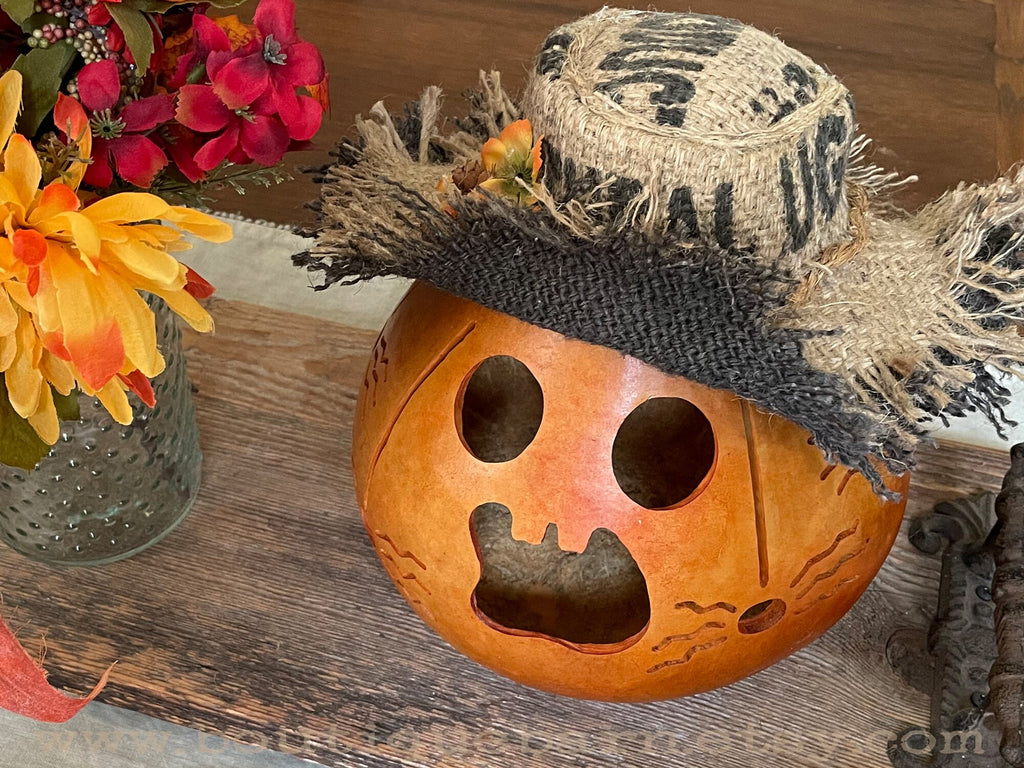 Decorative pumpkin with a straw hat on a wooden surface with flowers in the background.