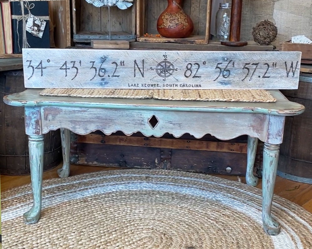 Antique table with a wooden sign displaying coordinates in a rustic setting.
