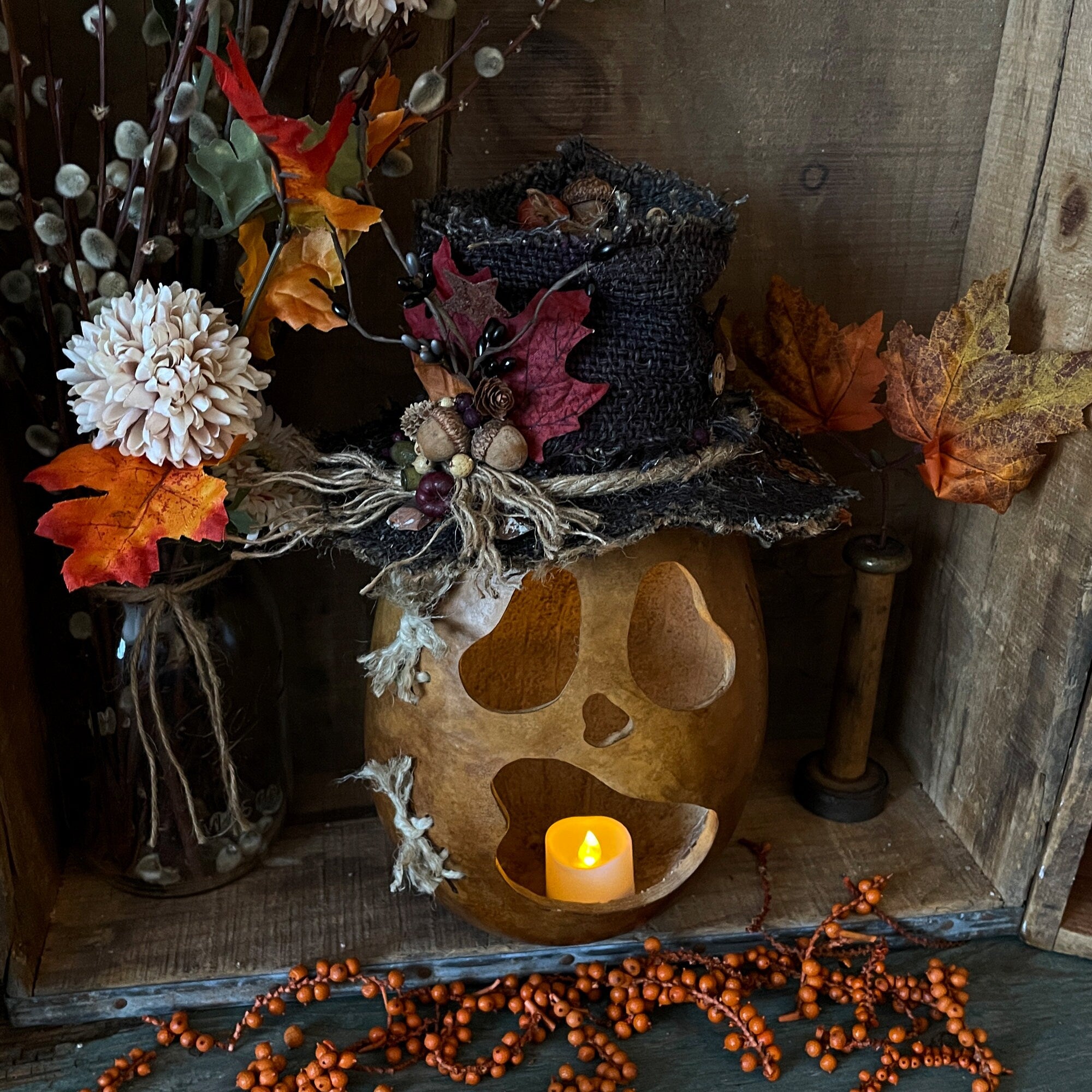 Decorative arrangement with a candle, autumn leaves, and a wooden skull on a rustic surface.