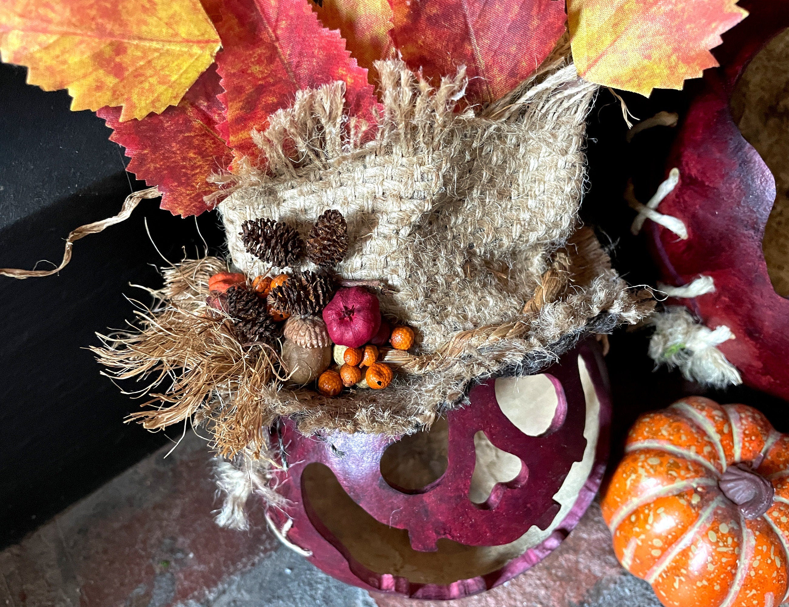 Decorative wreath with autumn leaves, pinecones, and pumpkins on a dark surface.