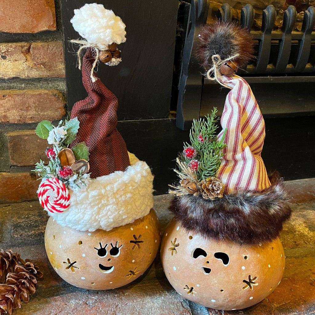 Two decorative pumpkins with faces and festive hats on a stone surface.