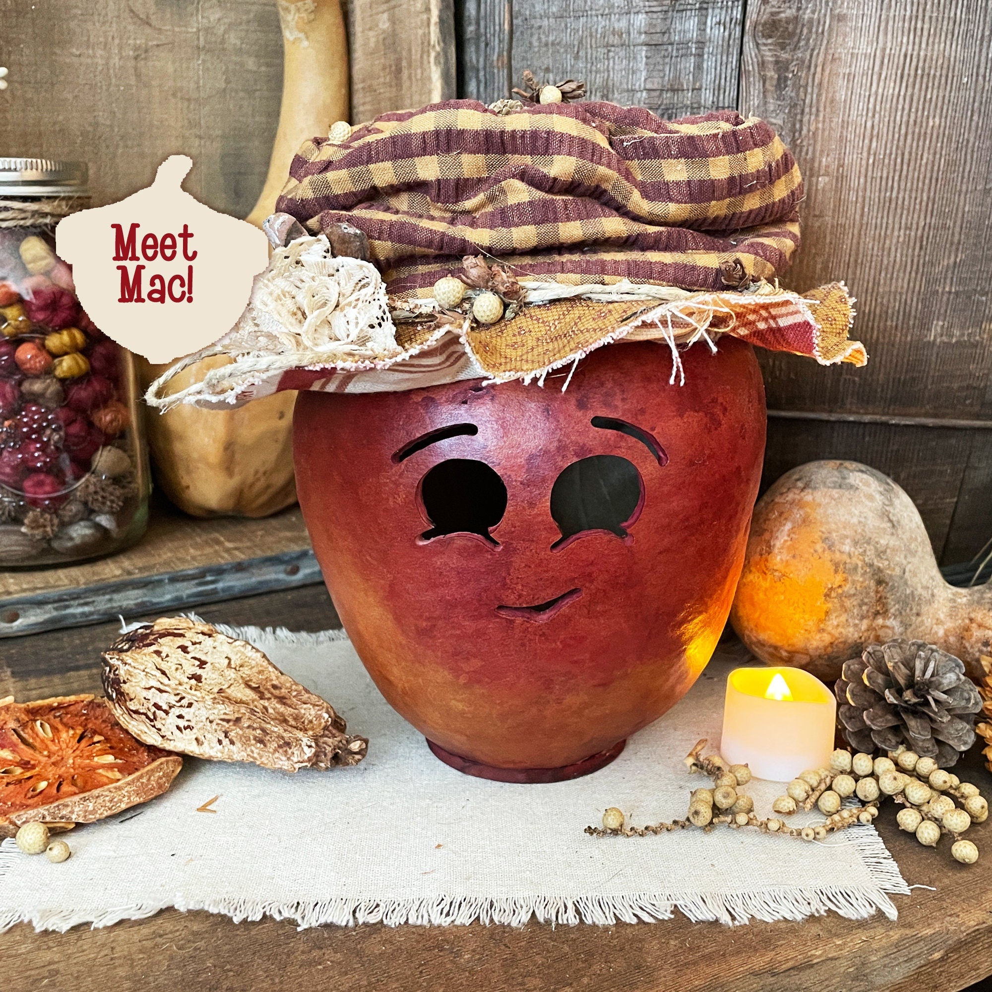 Decorative jar with face and plaid hat on a rustic wooden surface with pumpkins and candles.