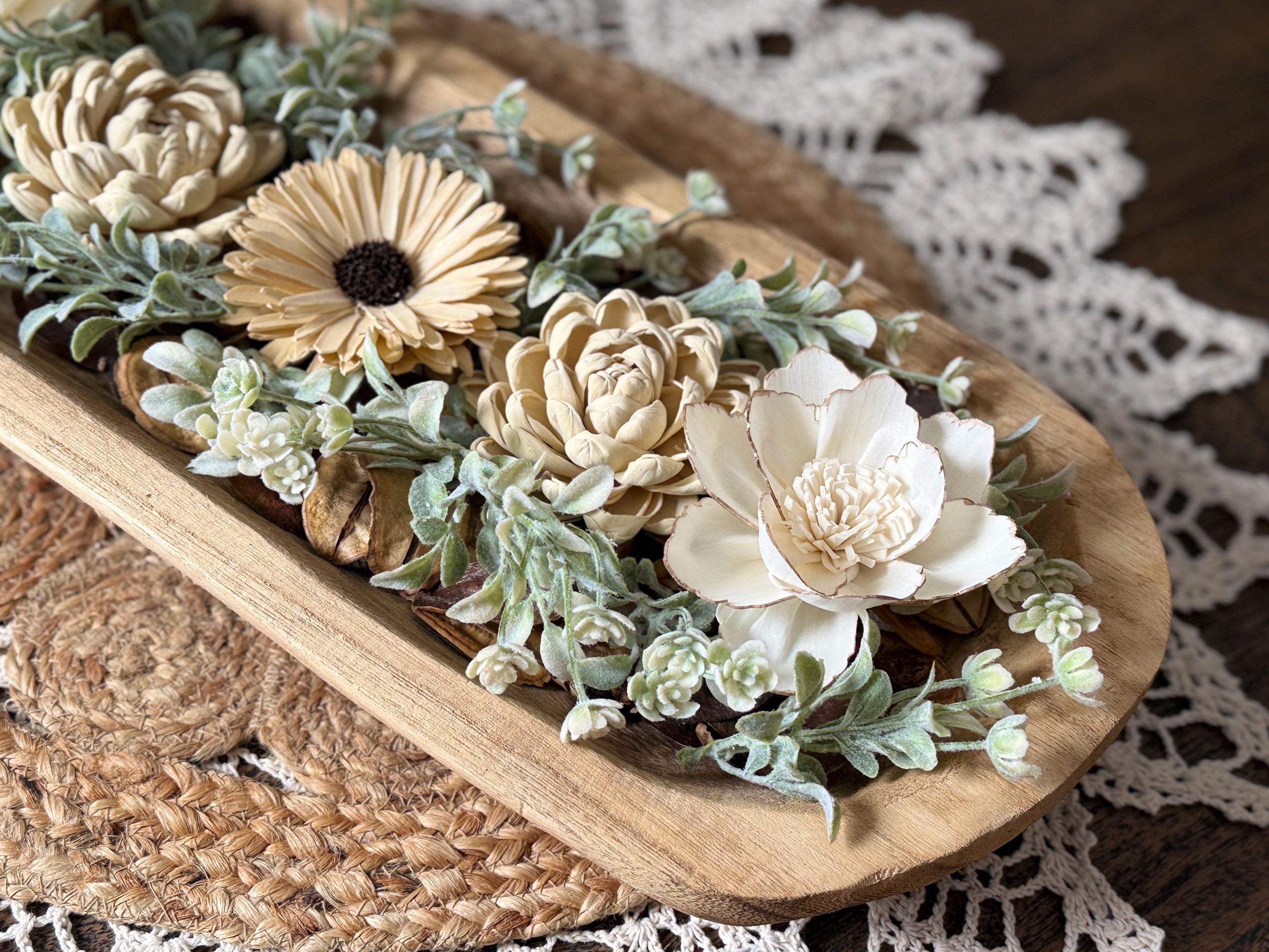 Decorative arrangement of flowers and plants a wooden dough bowl with a lace doily in the background.