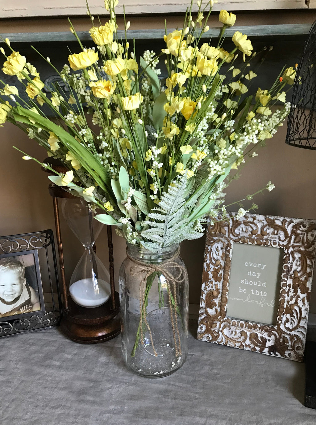 Bouquet of yellow flowers in a glass jar on a surface with decorative items in the background.