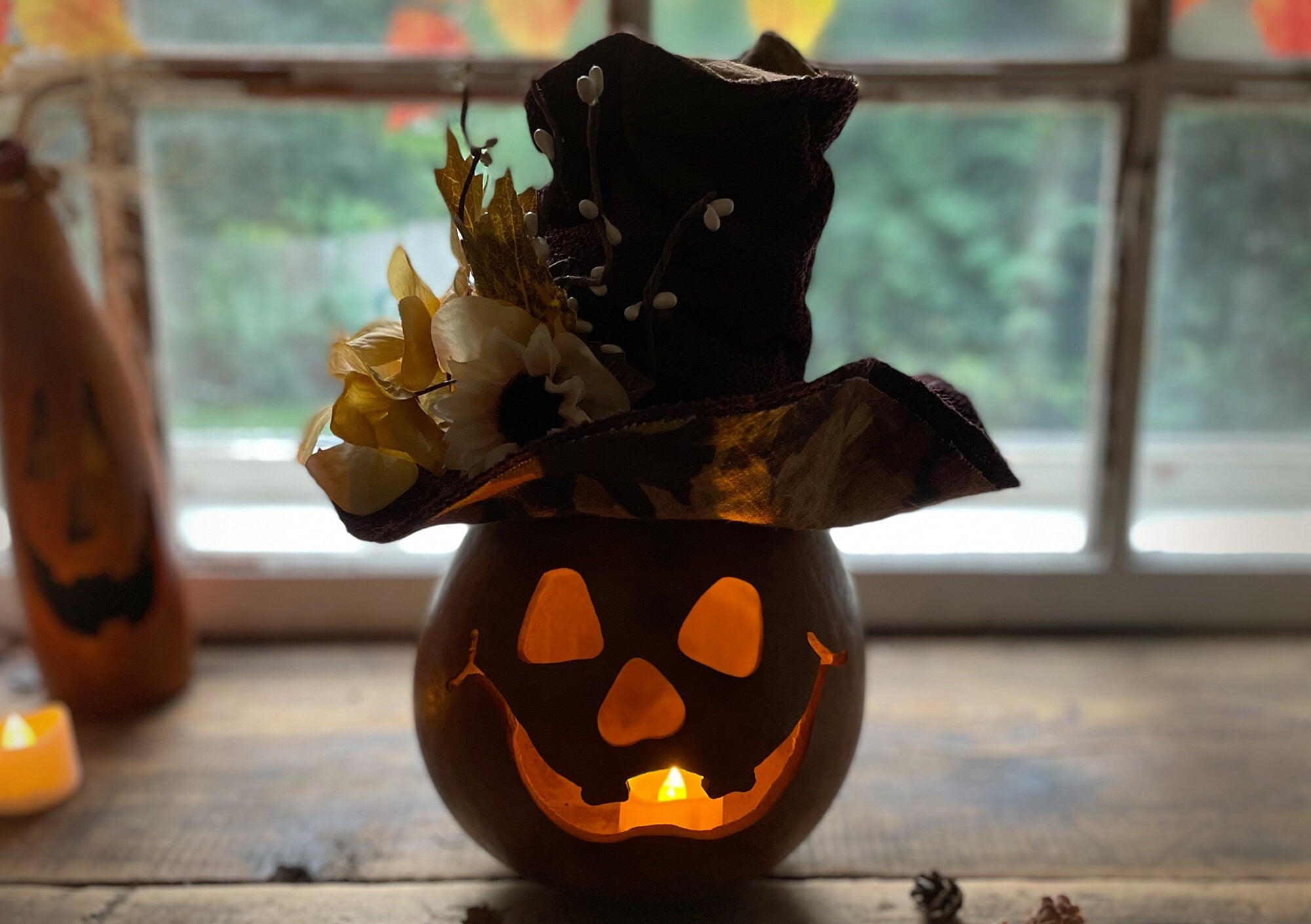 Decorative gourd with jack-o'-lantern face and bat wings on a wooden surface.