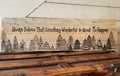 Wooden sign with engraved trees and text 'Always Believe That Something Wonderful Is About To Happen' on a wooden surface.