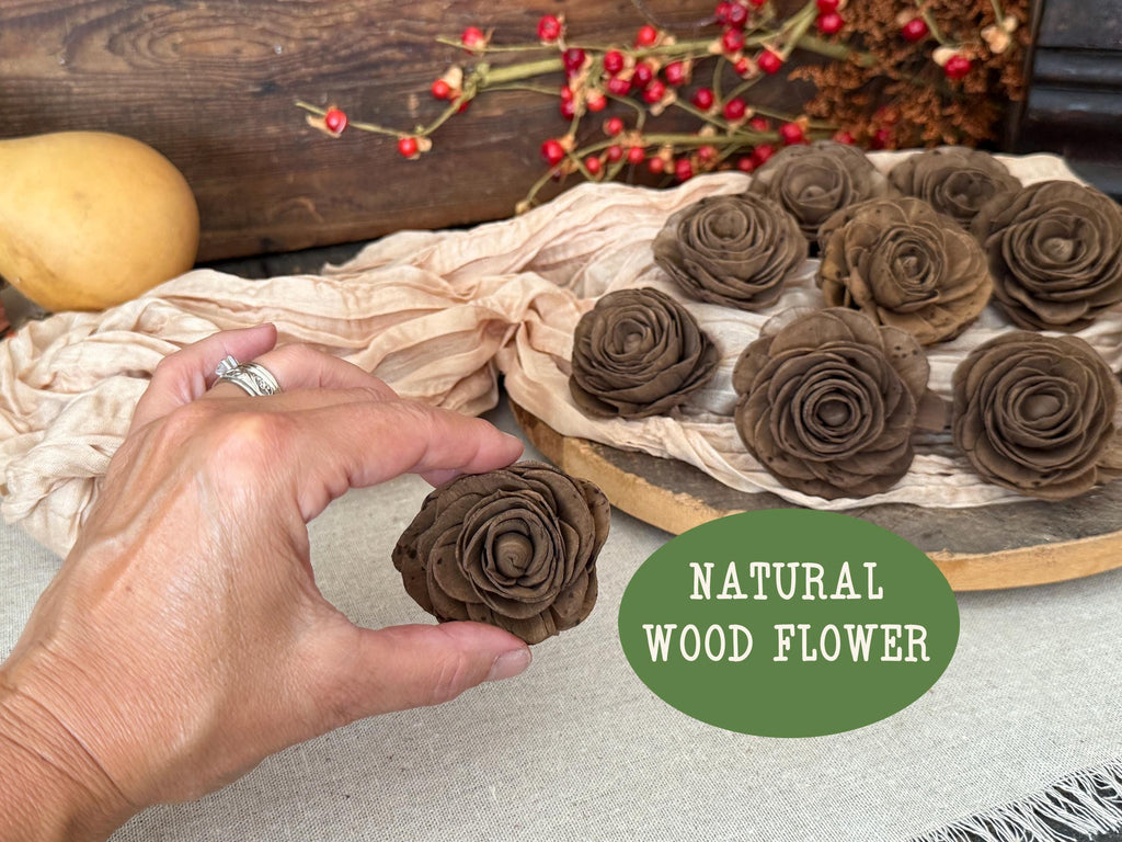 Hand holding a brown wooden flower with a tray of similar flowers and a decorative background.