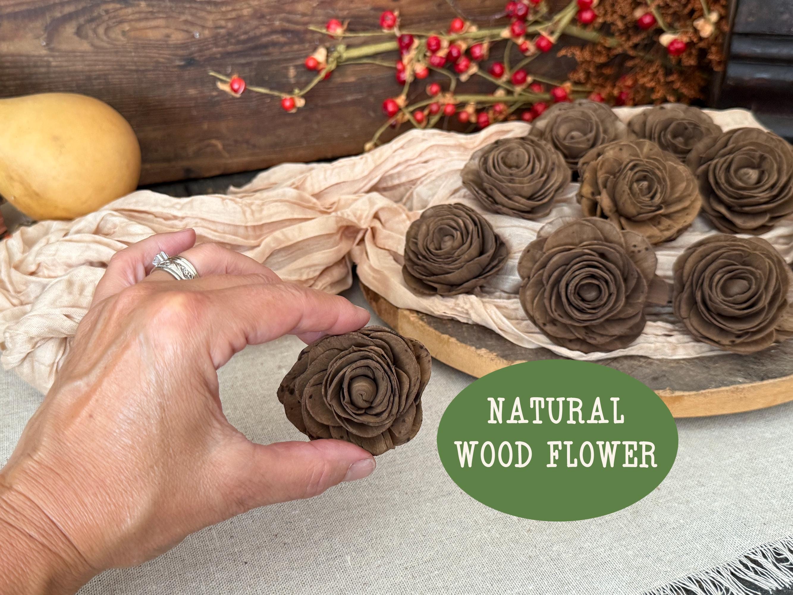 Hand holding a brown wooden flower with a tray of similar flowers and a decorative background.
