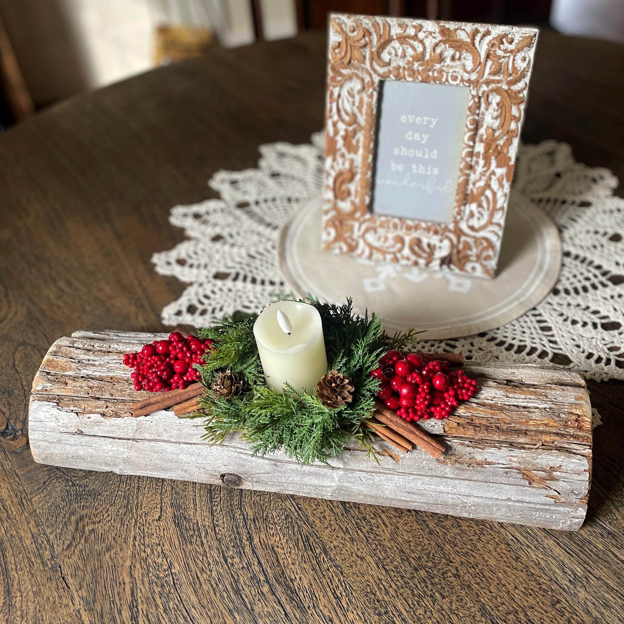 Decorative log centerpiece with candle, berries, and cinnamon sticks on a table with a lace doily.