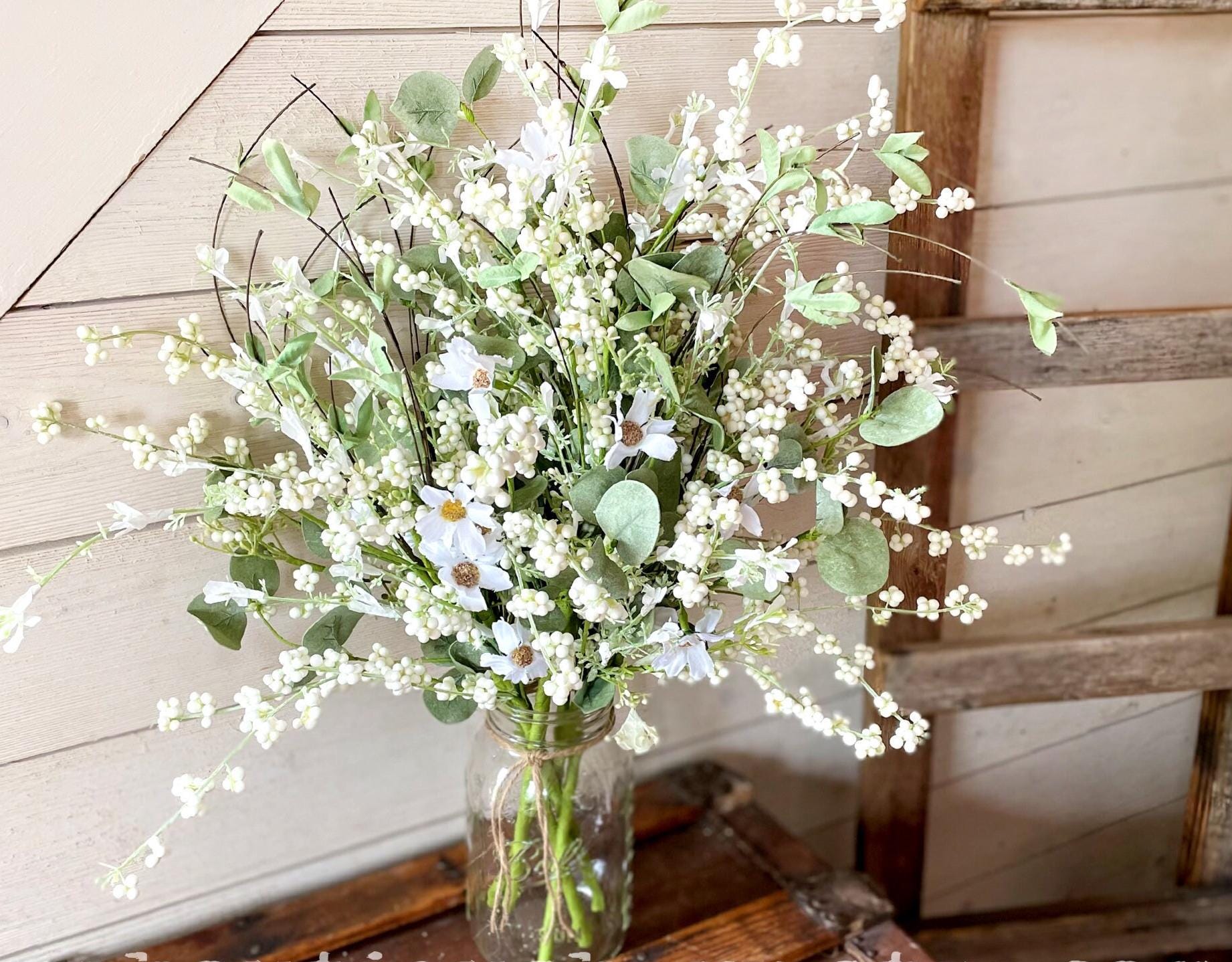 Bouquet of white flowers in a glass jar on a wooden surface with a rustic background.