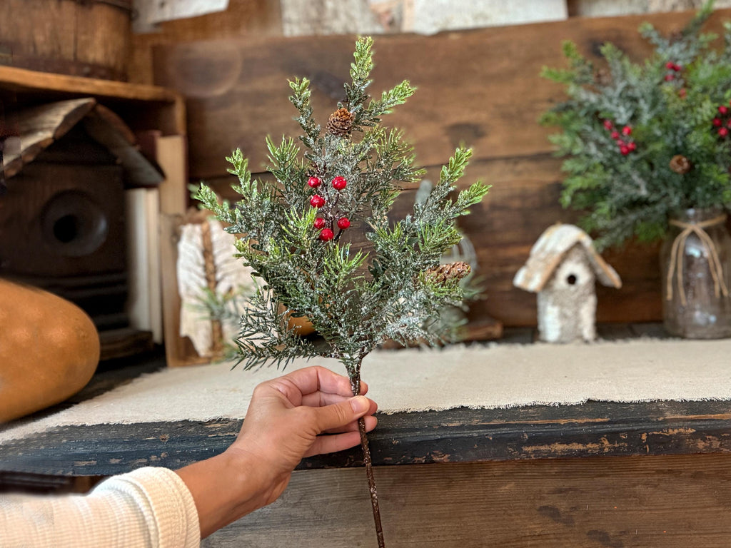 Hand holding a small artificial Christmas tree with red berries against a rustic wooden background.