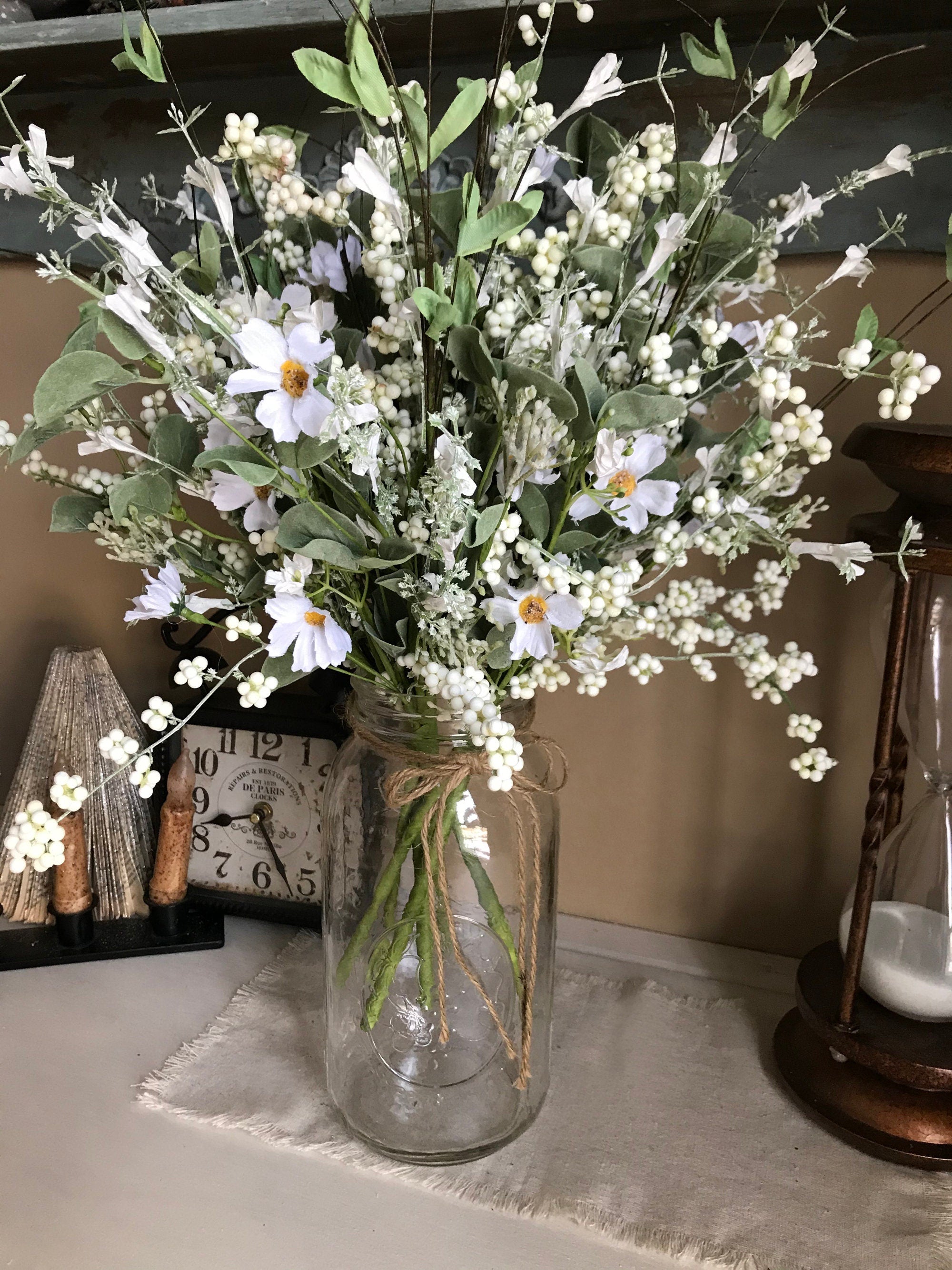 Clear glass vase with a bouquet of white flowers on a surface.