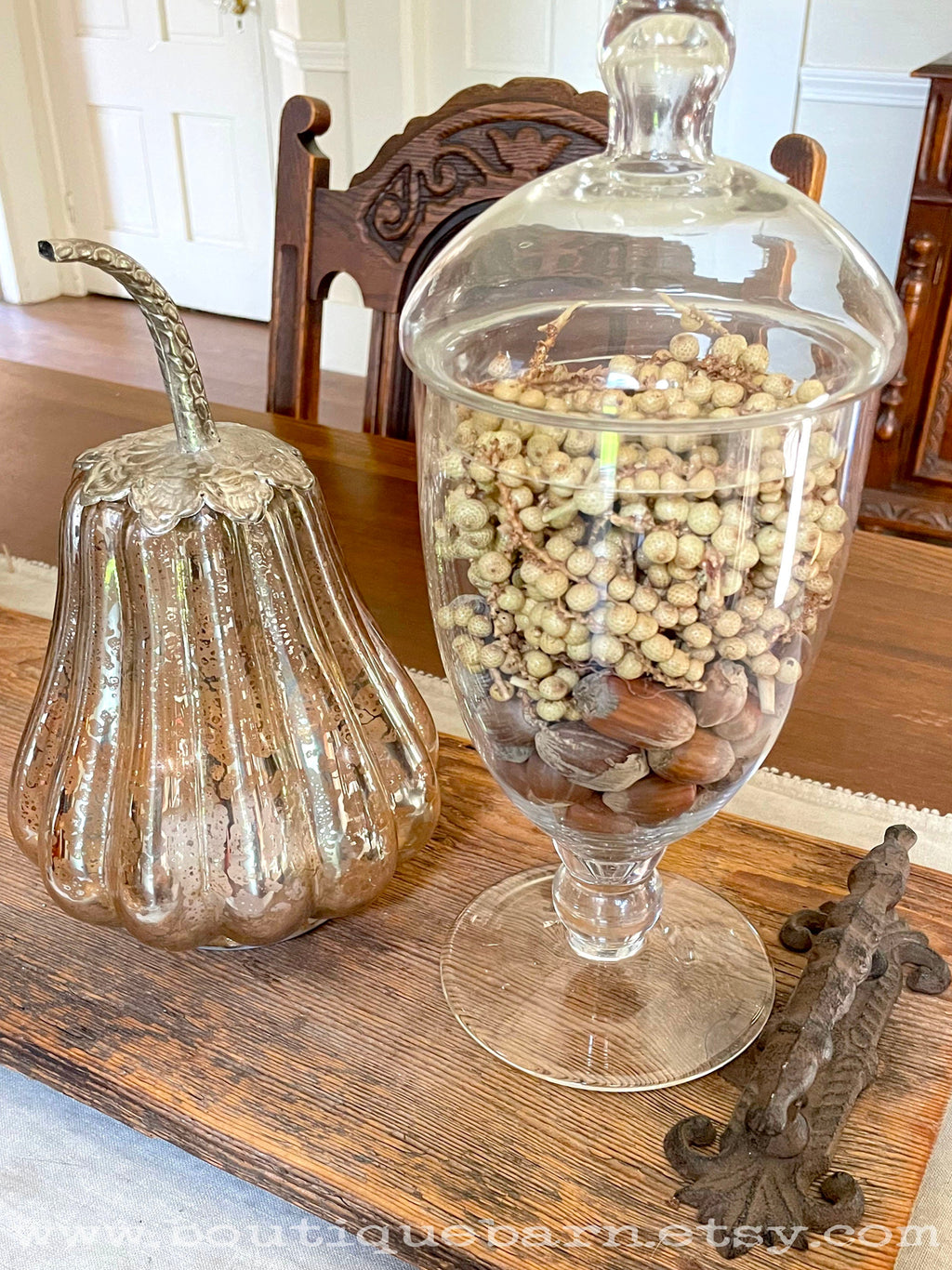Decorative glass container with dried canella berries and a glass pumpkin on a wooden table.