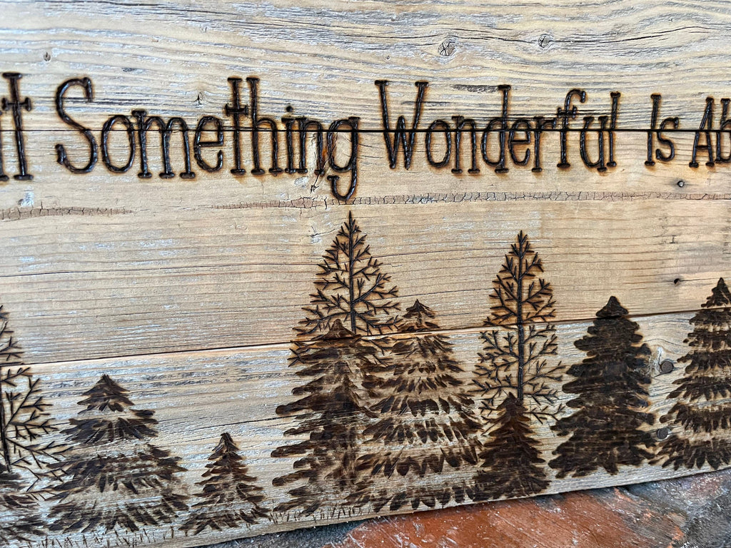 Wooden sign with engraved trees and text 'It Something Wonderful Is Ab', rustic background