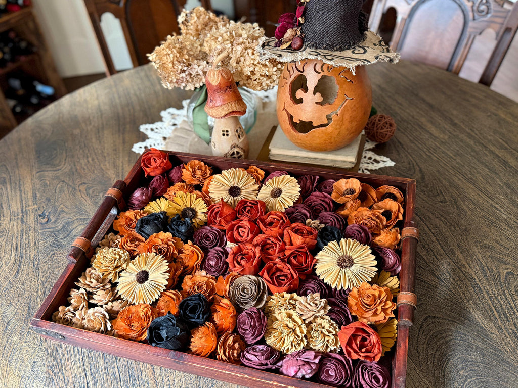 Decorative tray with assorted wood flowers, pumpkin, and small mushroom house on a wooden table.