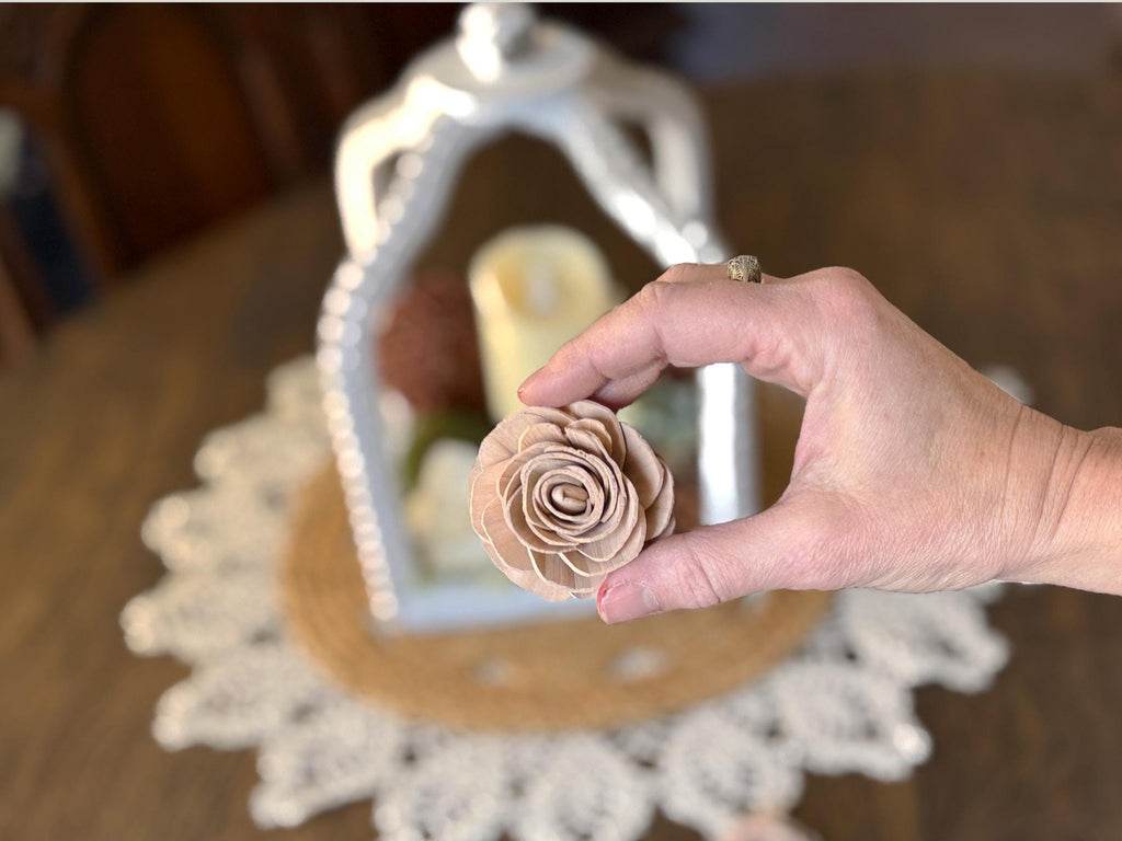 Hand holding a beige wood flower- with a decorative white lantern in the background.
