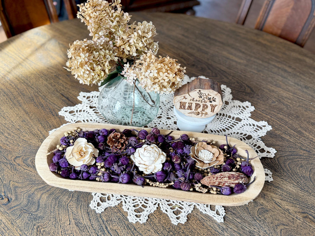 Decorative dough bowl arrangement with flowers and a small sign on a wooden table.