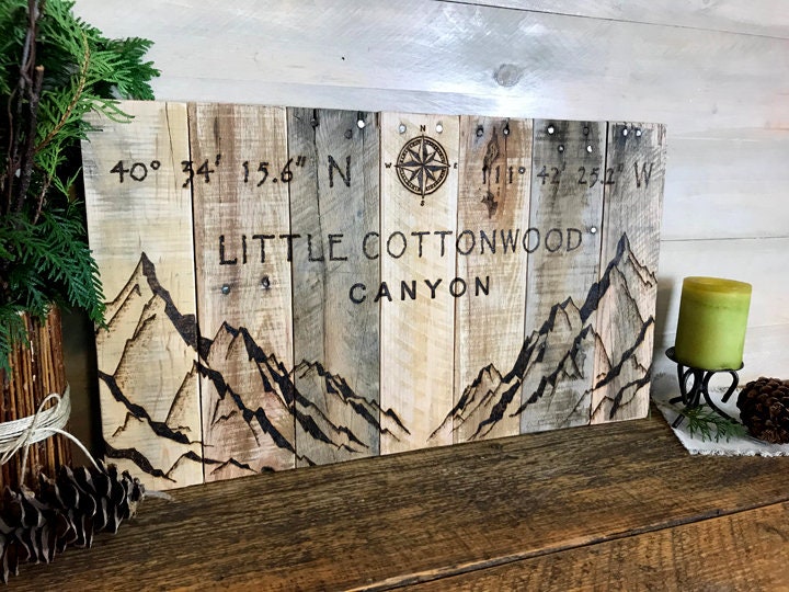 Wooden sign with mountain design and 'Little Cottonwood Canyon' text on a wooden surface.